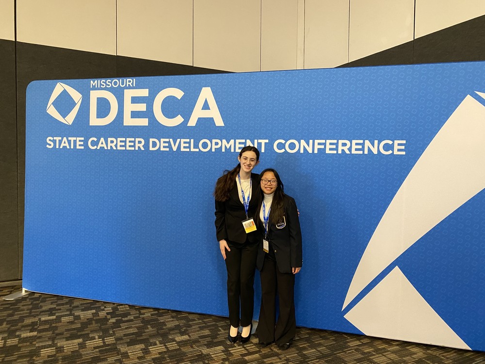 Hana and Hanna in front of DECA conference backdrop